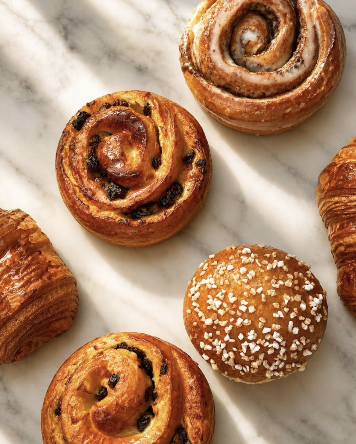 Pain aux raisins, cinnamon roll and pearl-sugar brioche on marble