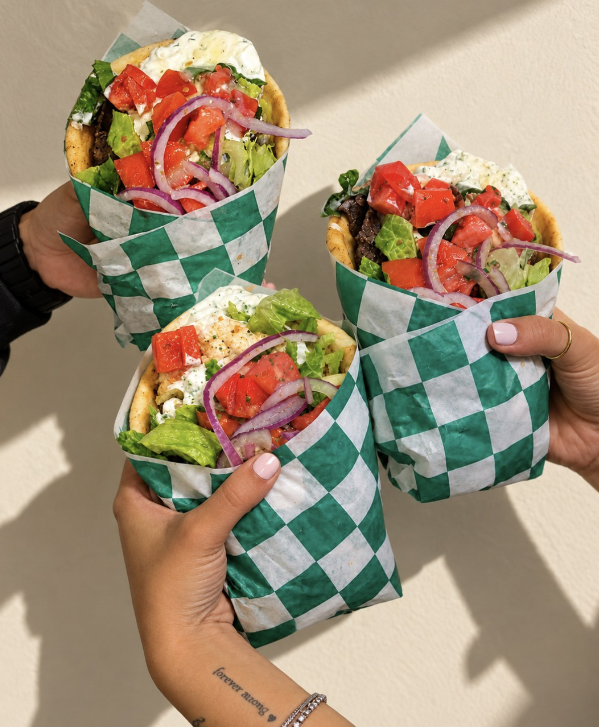 Three pita wraps held up against a sunlit wall