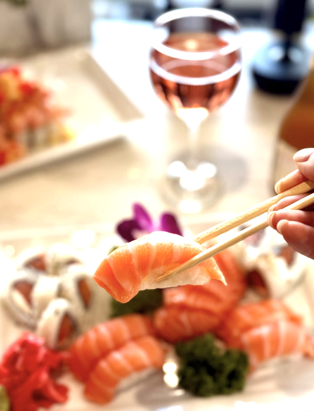 Salmon nigiri held in chopsticks with rosé behind